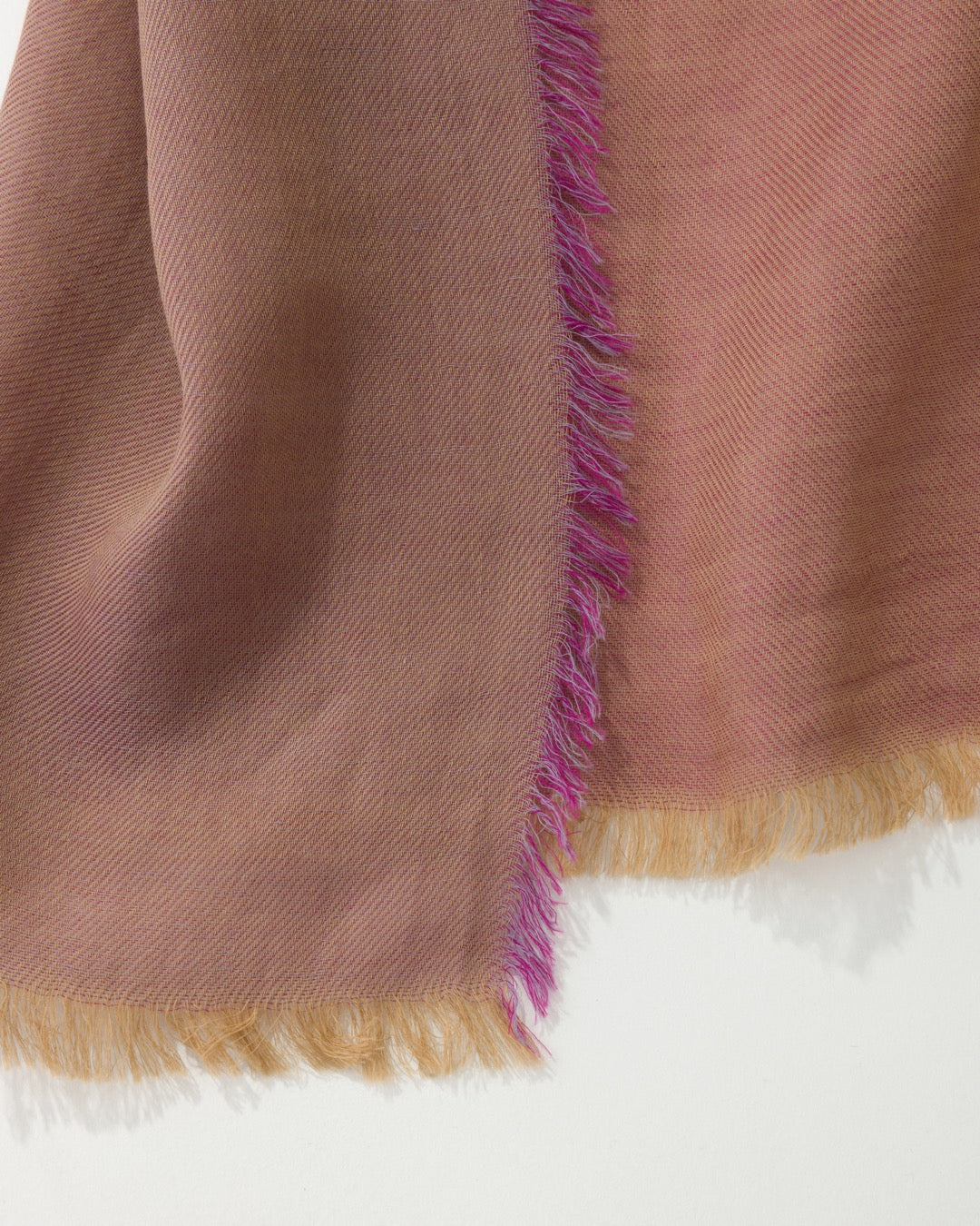 Detail of a dark pink scarf with purple and gold trims against a white background