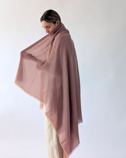 A woman wearing a pink shawl draped over her shoulders, paired with light beige trousers, photographed against a clean white studio background.