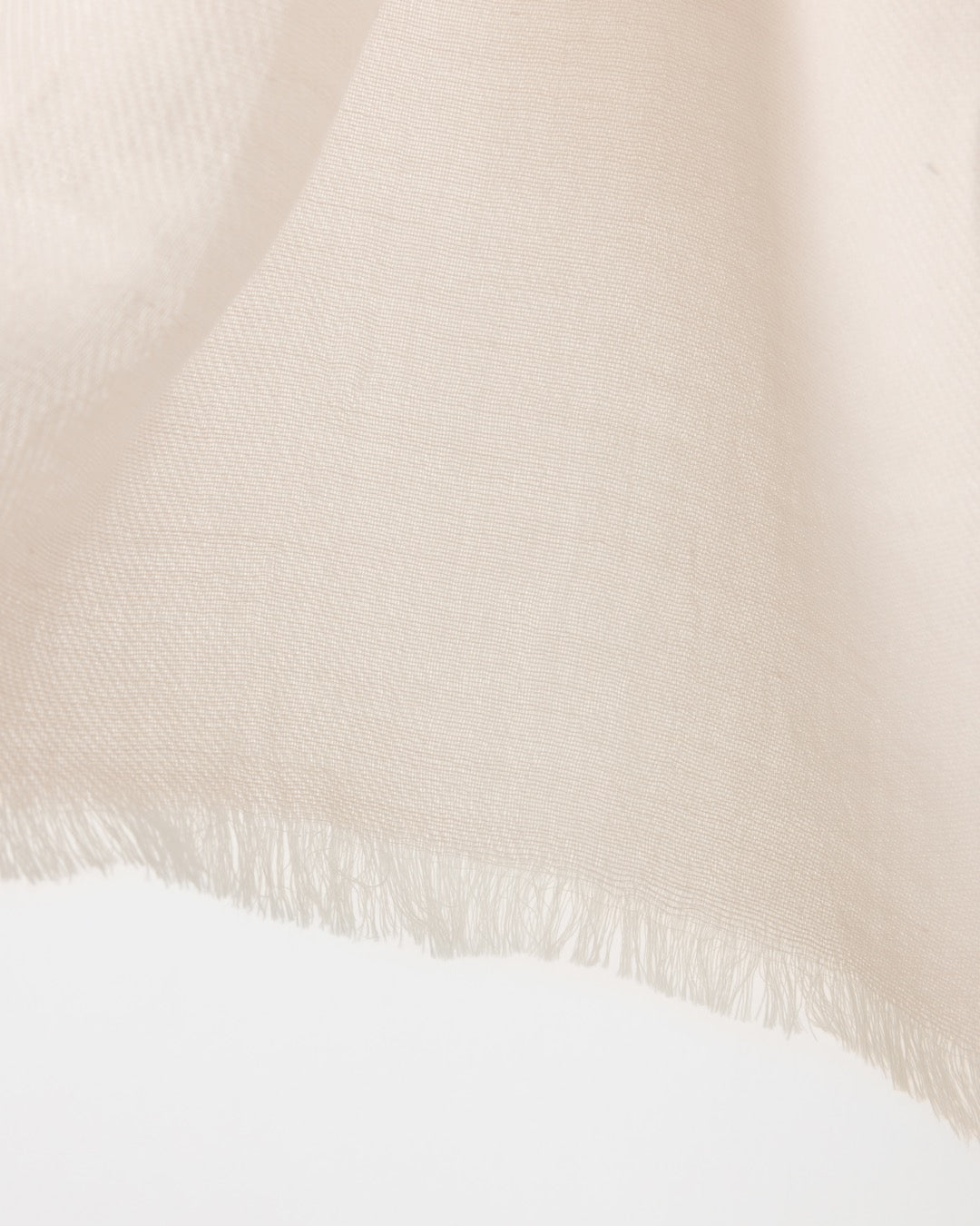 Detail of a white-coloured fringed scarf on a white background.